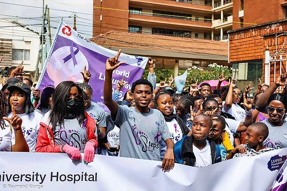Walkers raising their hands behind the Aga Khan University Hospital banner at the start of the World Lupus Day 2026 walk